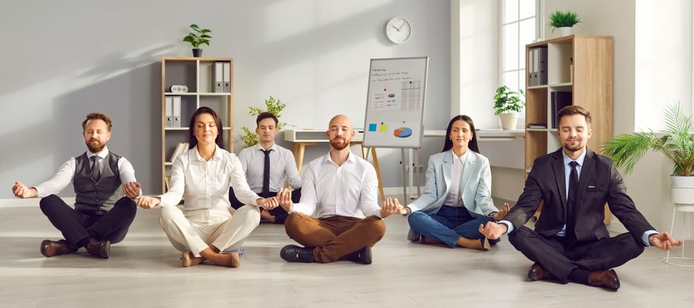 Office employees taking part in a workplace yoga session, representing staff wellbeing and the importance of reviewing company pension schemes for SMEs.